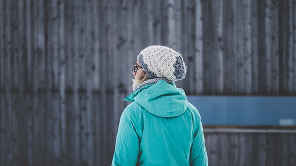 a young women stands with her back to you and wears a mint green jacket and knitted ice cap and also part of her glasses are shown in the image