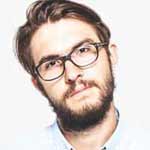 a man wearing black glasses and has a brown hair he is looking directly at you while leaning his head to the left 